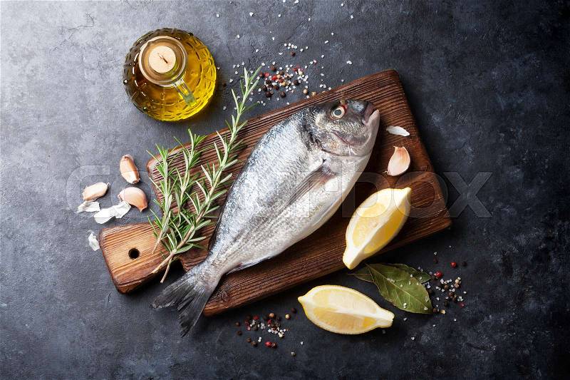 Raw fish cooking and ingredients. Dorado, lemon, herbs and spices. Top view on stone table, stock photo
