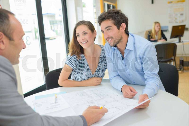 Architect drawing up plans with young couple, stock photo