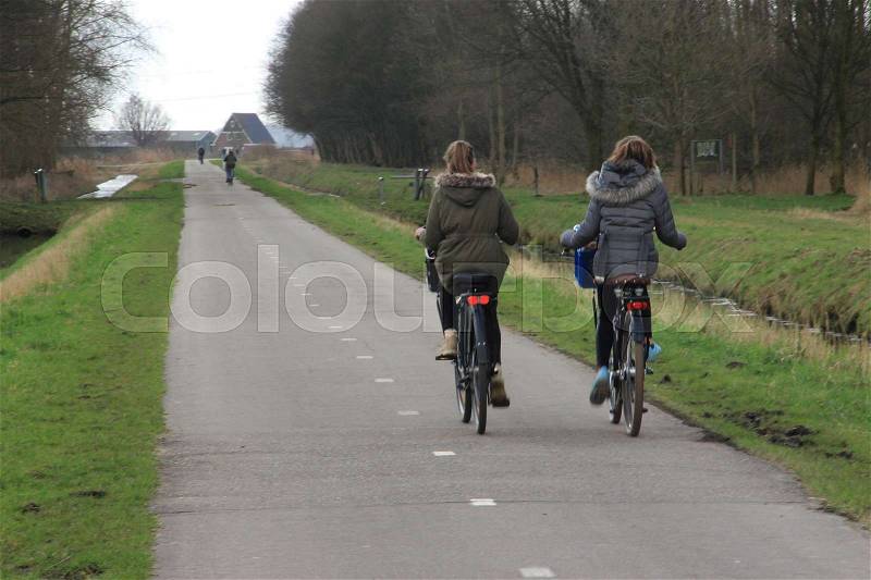The two schoolgirls are going home and cycling on the bike path in the park at the country side in the soft winter, stock photo