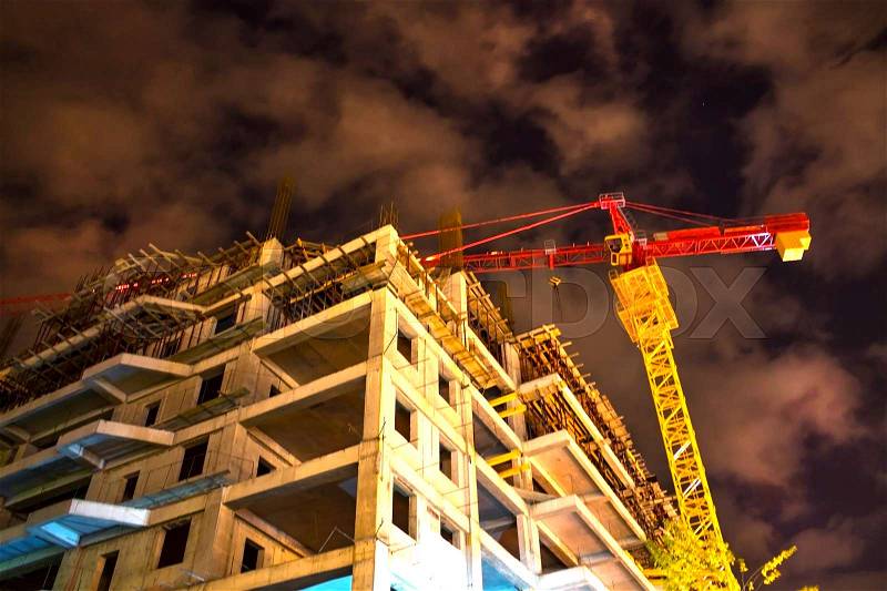 Unfinished building and hoisting crane at night time, stock photo