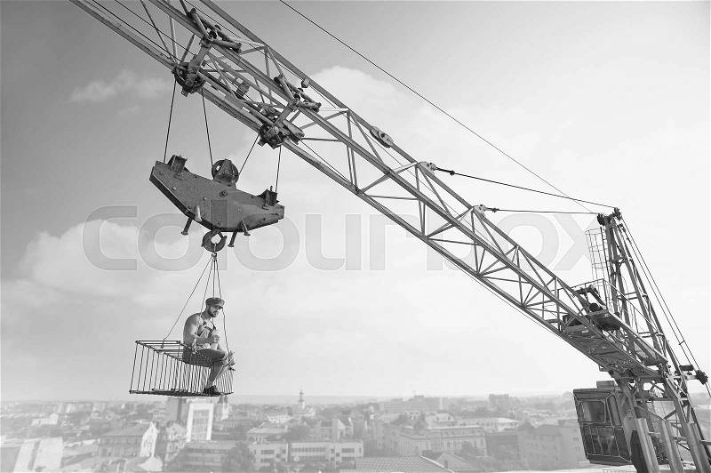 Extreme lunch. Black and white shot of an old fashioned shirtless relaxed construction worker having lunch sitting on a crossbar hanging from the crane high above the city development construction, stock photo