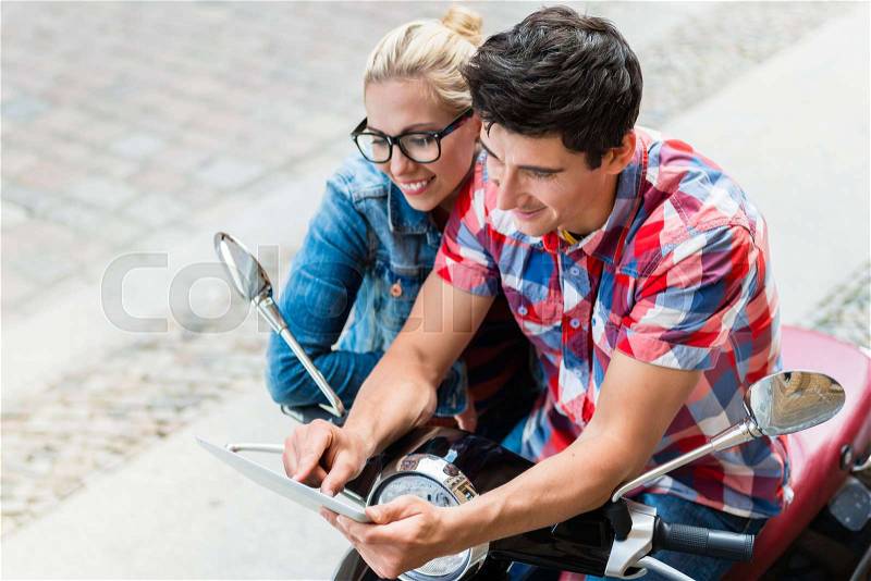 Young Couple, woman and man, on city trip in Berlin planning their Vespa tour using tablet PC, stock photo