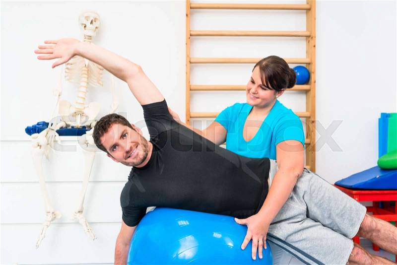 Young man exercising on swiss ball in physiotherapy, stock photo
