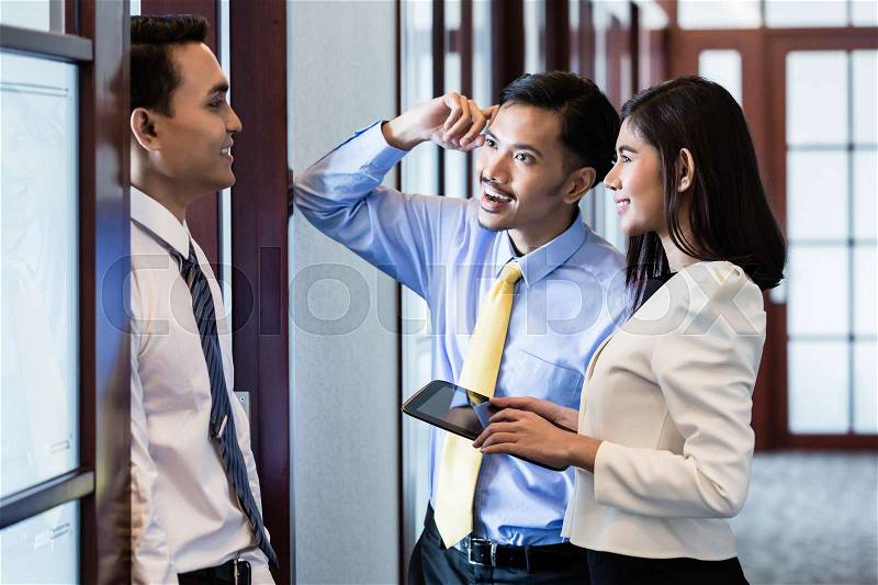 Indonesian co-workers, men and woman, in office hallway talk about business project, stock photo