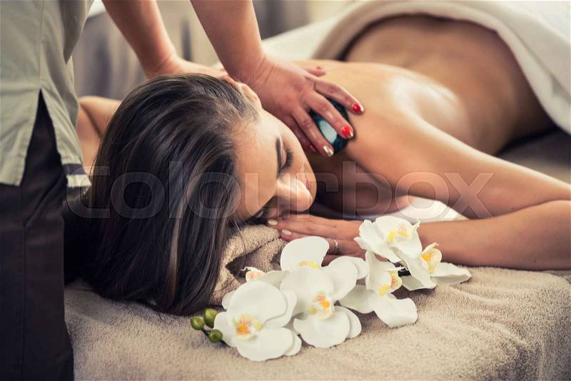 Young woman enjoying the therapeutic effects of a traditional hot stone massage at luxury spa and wellness center, stock photo