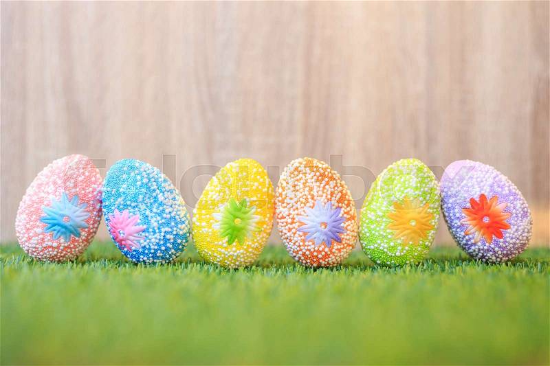 Artificial color eggs on green grass with wooden wall background. For Easter day use, stock photo