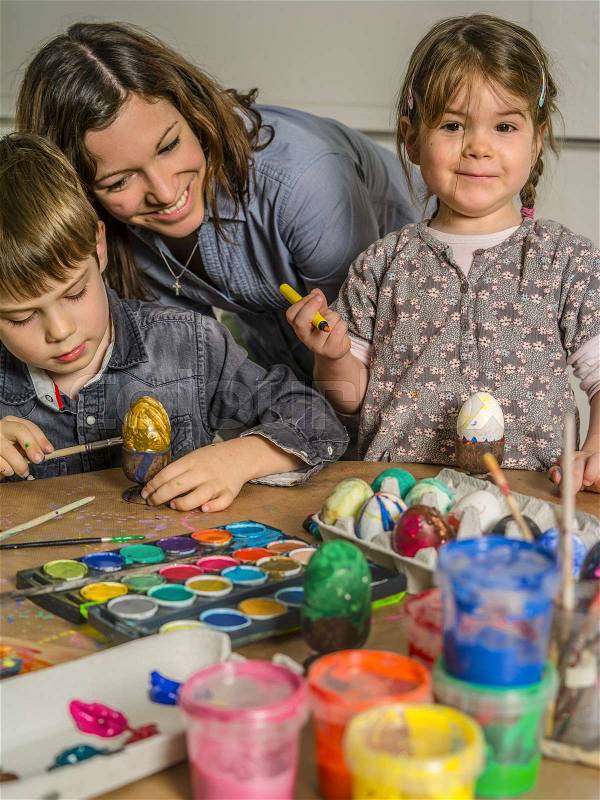 Photo of a mother and her children painting and decorating hard-boiled eggs for easter, stock photo