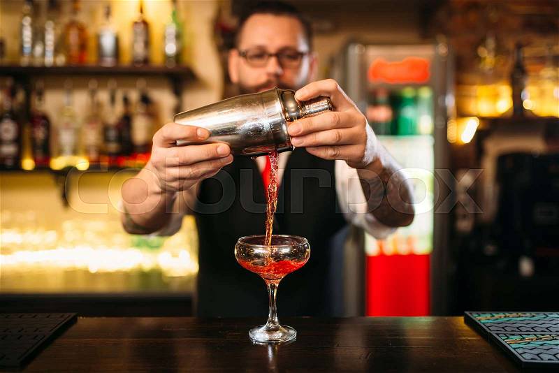 Barman is making alcohol cocktail at bar counter. Barman with shaker and glass of beverage, stock photo