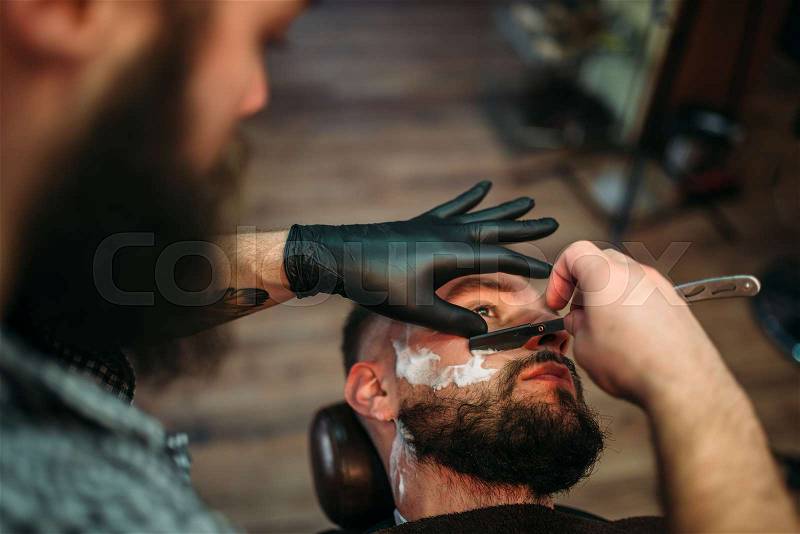 Barber shaves the beard of the client by straight razor at barbershop. , stock photo