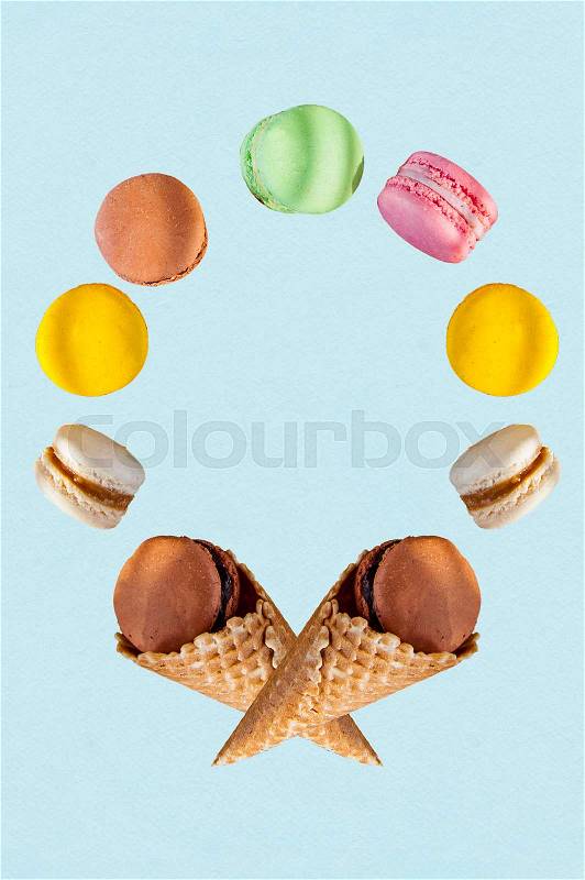 Multicolored cake macaron or macaroons and waffle cones in the form of round frame on the blue background. Top view. Free space for text, stock photo