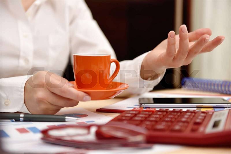 Woman hand with coffee cup and saucer. Paper with financial data in form of charts and diagrams, stock photo