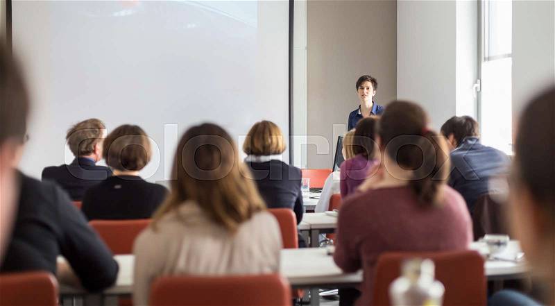 Female speaker giving presentation in lecture hall at university workshop . Participants listening to lecture and making notes. Scientific conference event, stock photo