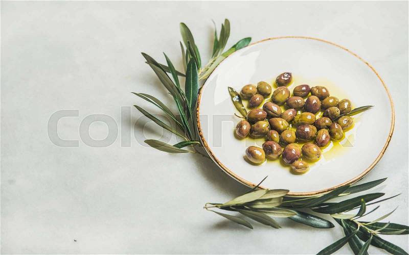 Pickled green Mediterranean olives in oil and olive tree branch, stock photo