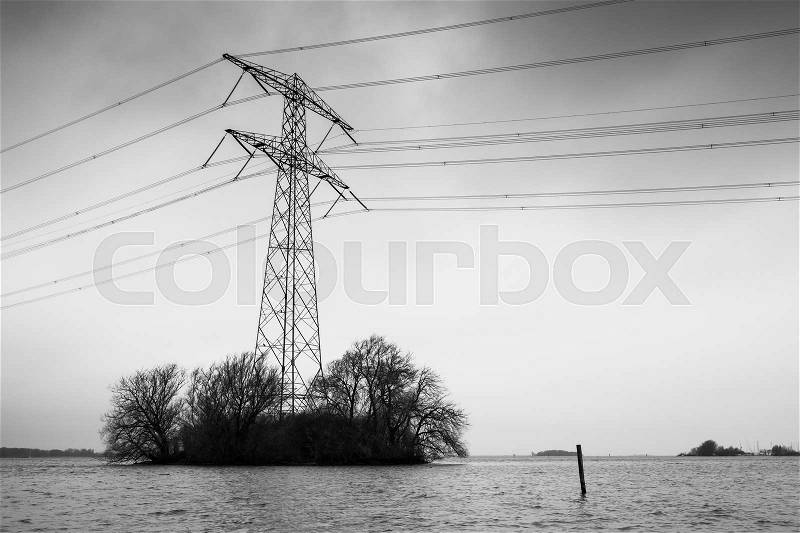 Transmission power tower, electricity pylon stands on small island with bare trees. Steel lattice tower, used to support an overhead power line. Black and white photo, stock photo