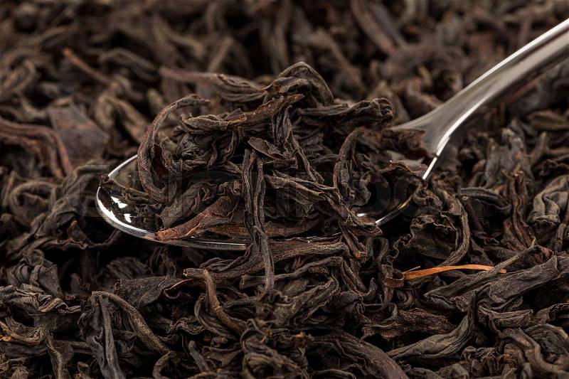 Black tea in a spoon on a black tea background. Close-up shot, stock photo