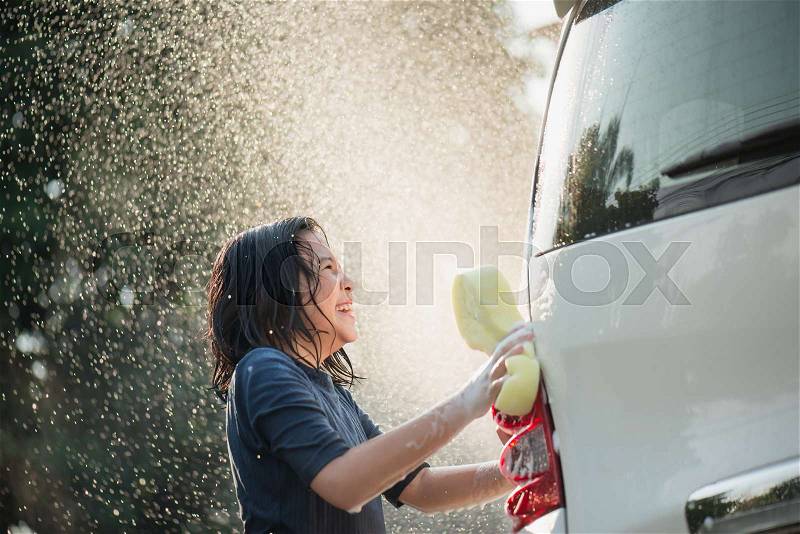 Asian girl washing car in the garden on summer day, stock photo