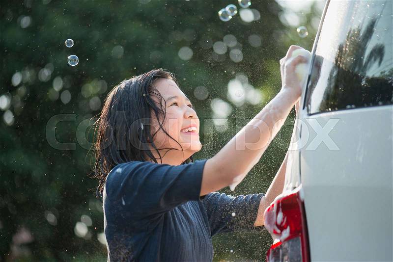 Asian girl washing car in the garden on summer day, stock photo