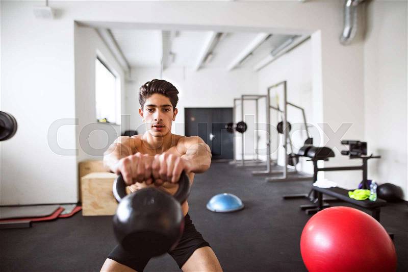 Fit hispanic man doing strength training, doing kettlebell swings in crossfit gym, stock photo