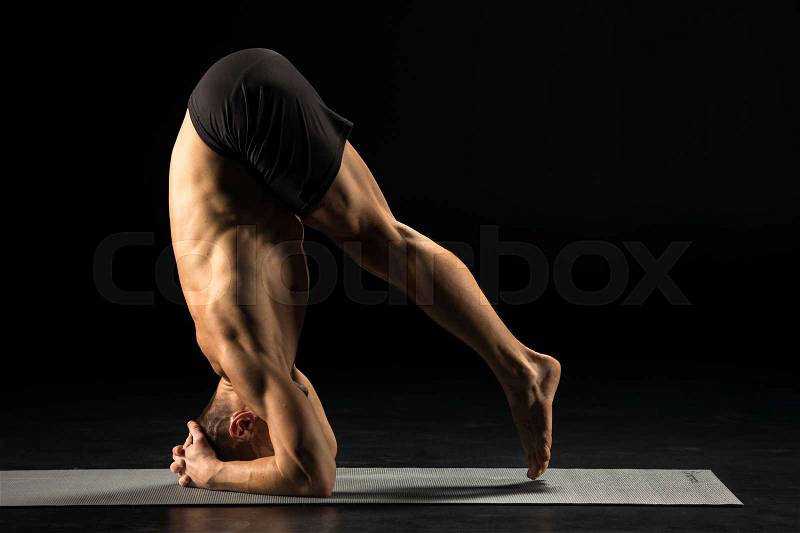 Man performing Sirsasana or Yogic Head Stand on yoga mat , stock photo