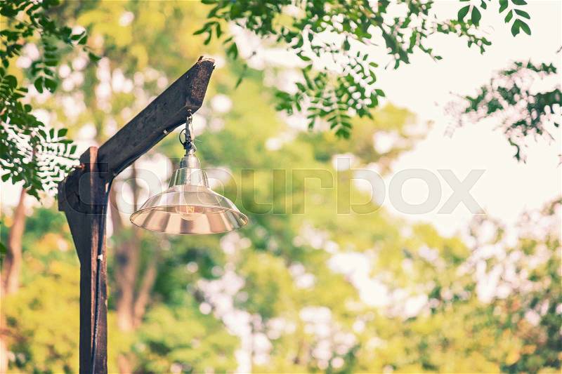 Simple basic lamp on old rustic wooden lampost against blurred trees and sky background, vintage cinematic color tone, room for copyspace, stock photo