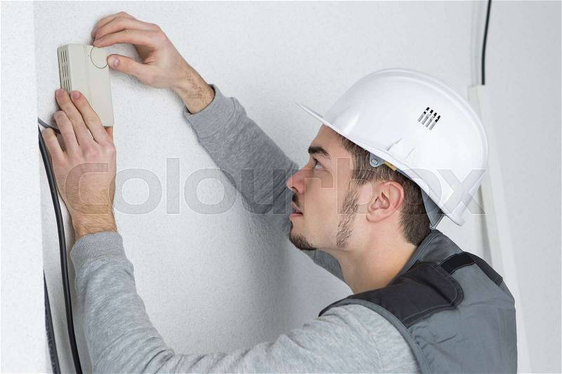Man fitting thermostat controller to wall, stock photo