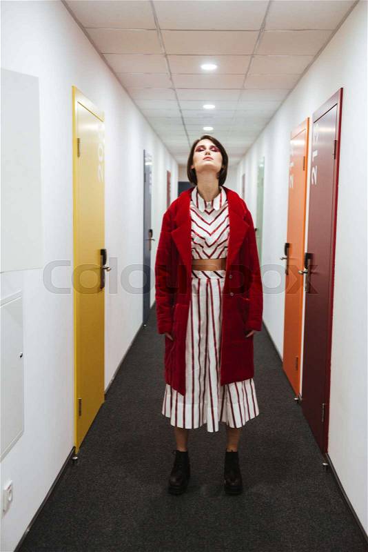 Attractive young woman in red coat standing in corridor, stock photo