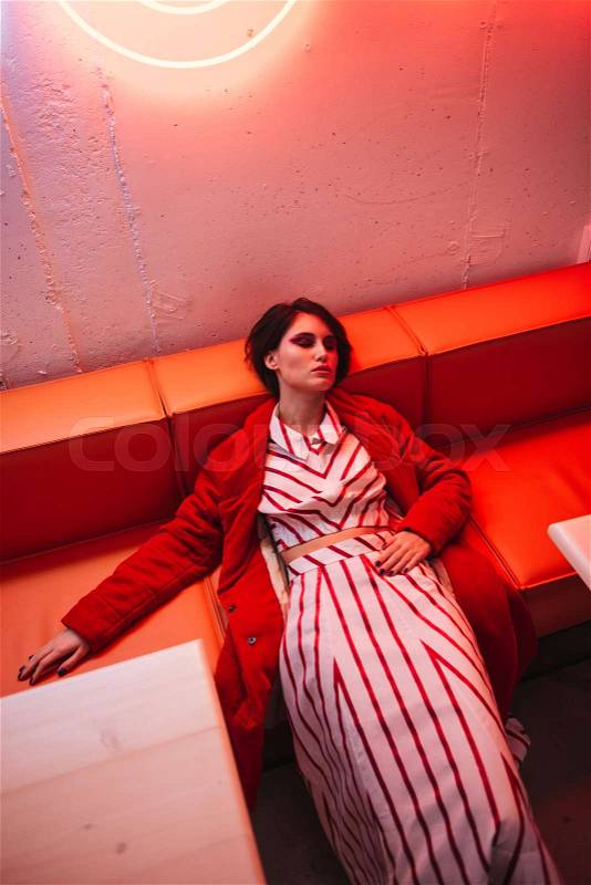 Tired fatigued young woman in red coat lying and sleeping in cafe, stock photo
