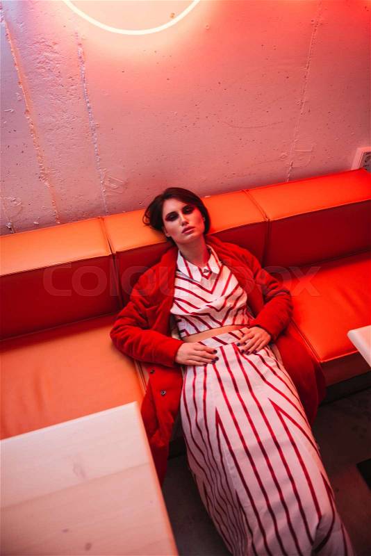 Exhausted beautiful young woman in red coat sleeping in cafe, stock photo
