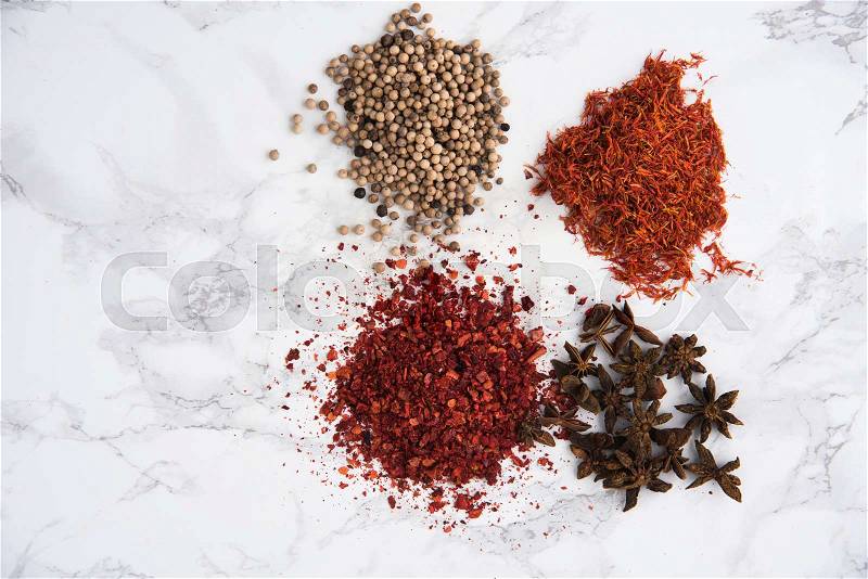 Top view of anise, white pepper, chilli pepper flakes and saffron heaps isolated on white marble background, stock photo
