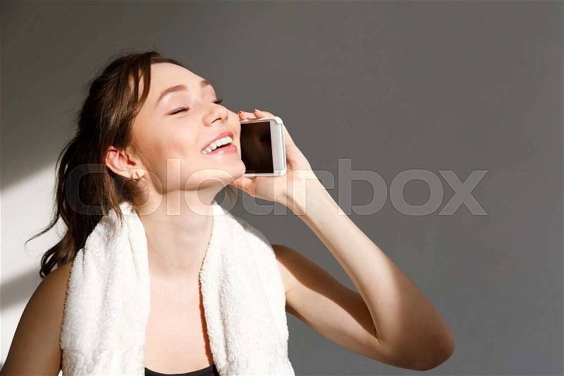Portrait of an attractive positive fitness girl talking on mobile phone over gray background, stock photo