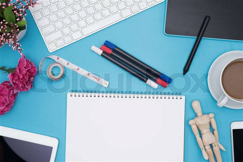 Professional graphic designer desk with computer, creative pen tablet, supplies, notebook, tablet, coffee cup, flower and wooden mannequin dummy on blue background, stock photo