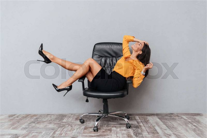 Happy business woman sitting on chair with hands up and having fun isolated over gray background, stock photo