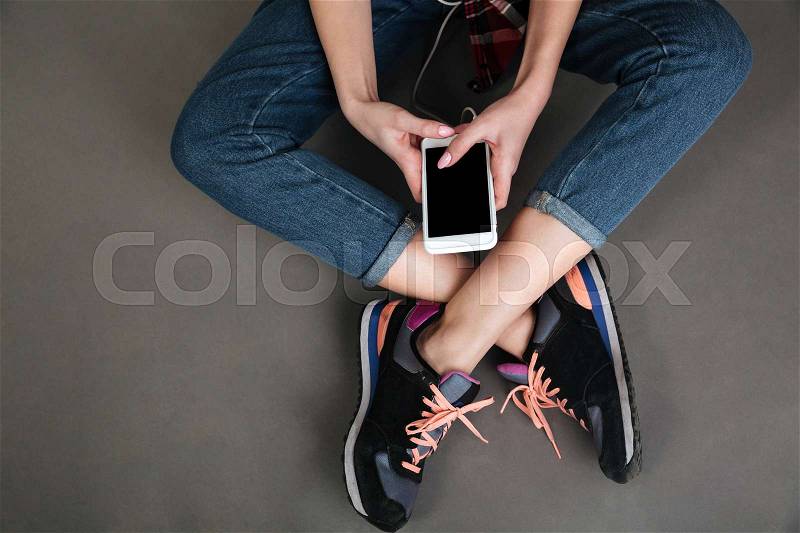 Close up portrait of a women crossed legs and hands holding blank screen mobile phone isolated on the gray background, stock photo