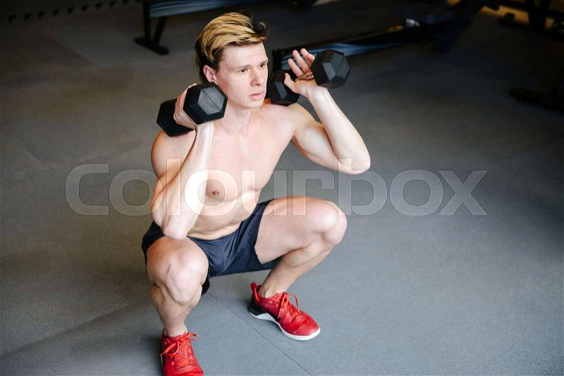 Top view of Muscular man with naked torso which doing exercise with dumbbells in gym, stock photo