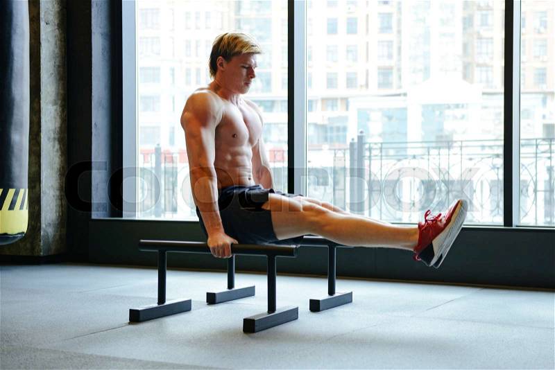 Athletic man which shakes the press on bars near the window in gym, stock photo