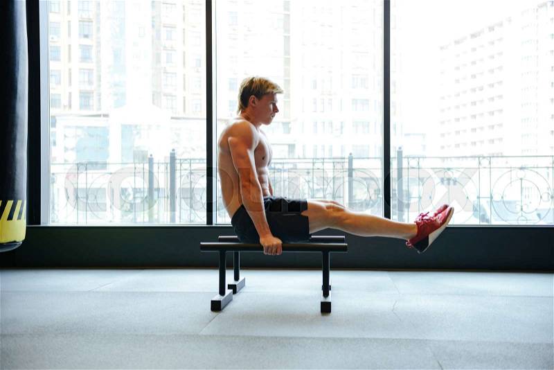 Side view of Athletic man which shakes the press on bars near the window in gym, stock photo