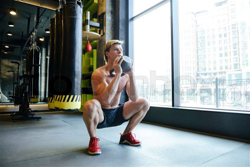 Young Athletic man which crouches with weight in gym, stock photo