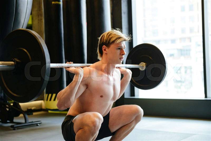 Young Athletic man with naked torso which crouches with barbell, stock photo