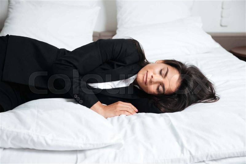 Portrait of a tired young businesswoman in suit laying on bed, stock photo