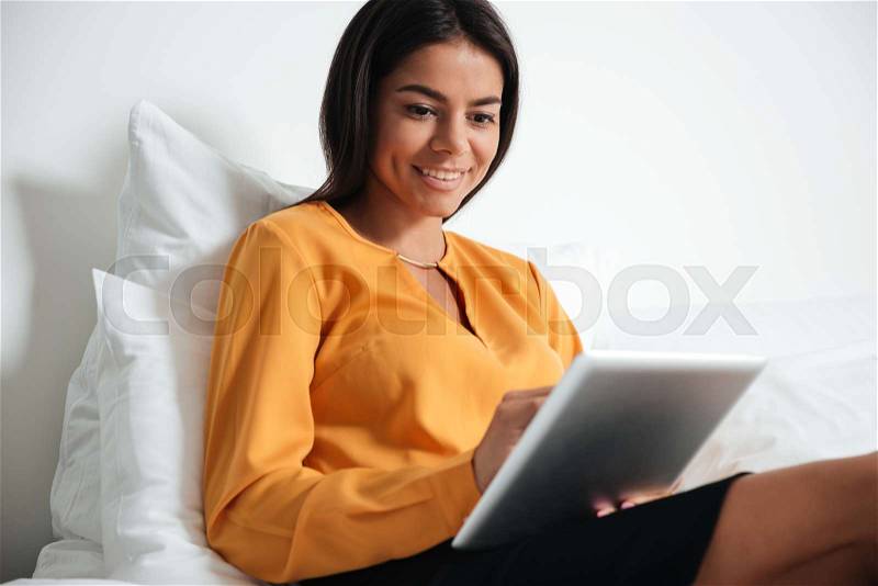 Happy businesswoman with tablet pc computer lying in hotel in bed, stock photo