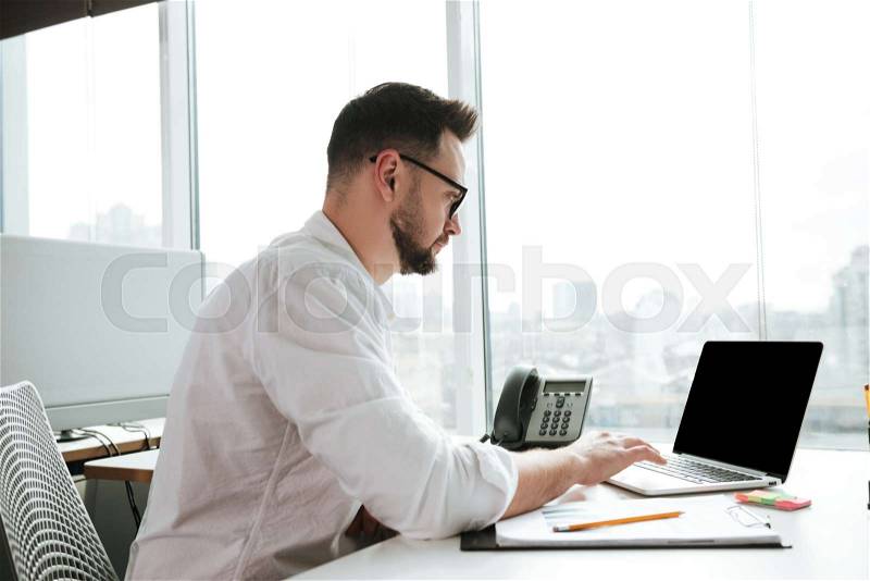 Side view of Man in shirt and eyeglasses which sitting by the table and using laptop computer, stock photo