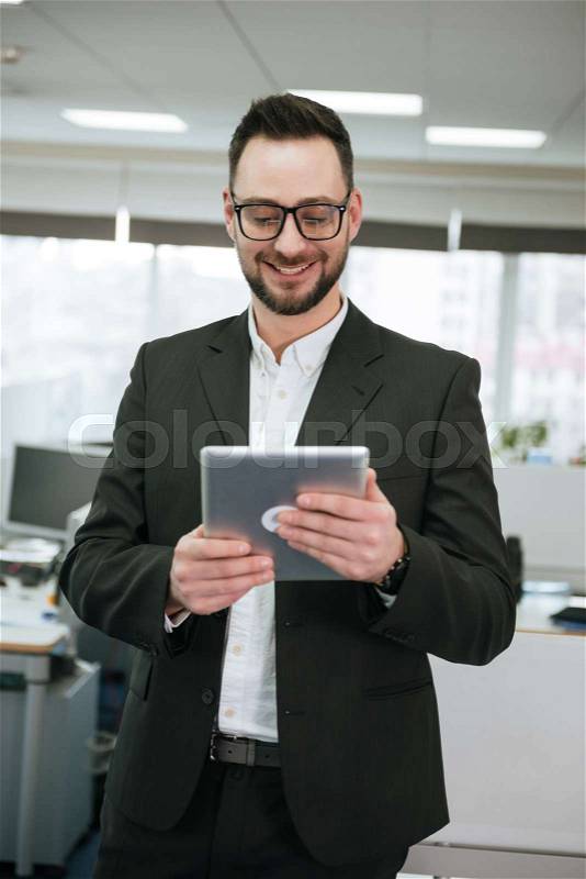 Vertical image of Bearded business man in suit and eyeglasses which using tablet computer in office, stock photo