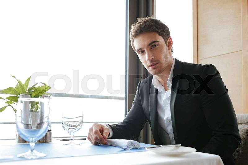 Side view of Calm Man in suit which sitting by the table in restaurant and looking camera, stock photo