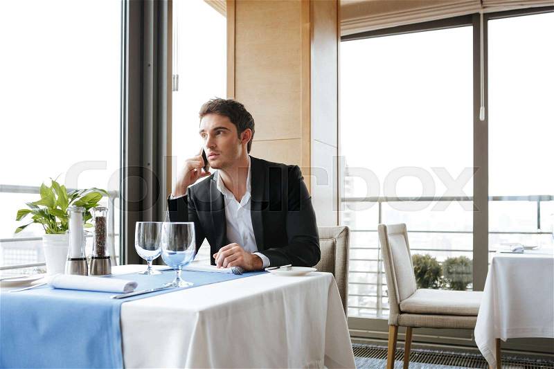 Calm Man in suit which sitting by the table in restaurant and talking on phone, stock photo