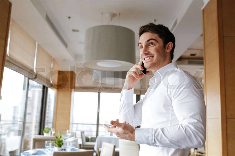 Side view of Happy man in shirt which standing in restaurant and talking on phone, stock photo