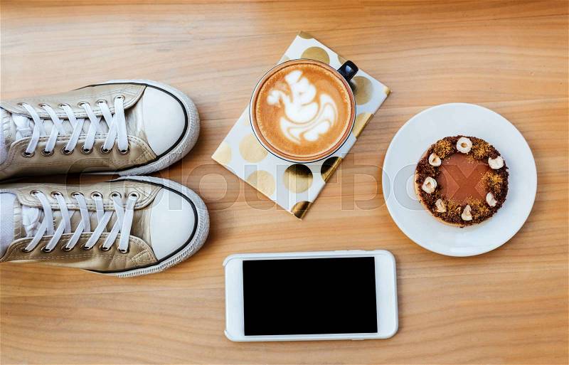 Top view of wooden board with phone, coffee, cake, gumshoes and notebook, stock photo