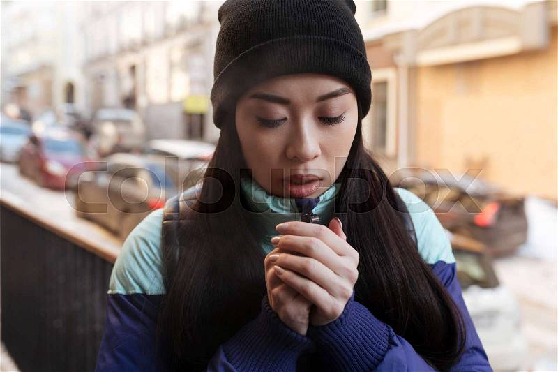 Frozen Asian woman in warm clothes which standing on the street and trying to keep warm, stock photo