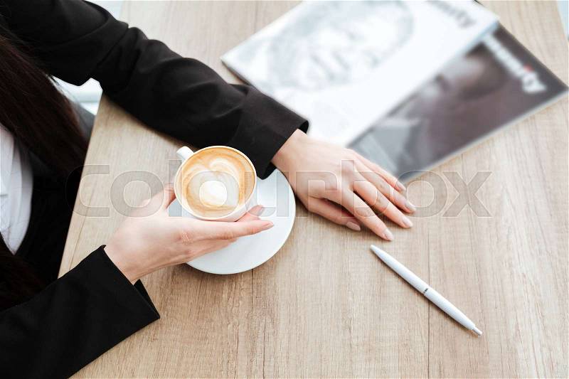 Top view of businesswoman sitting at the table and drinking coffee with milk, stock photo