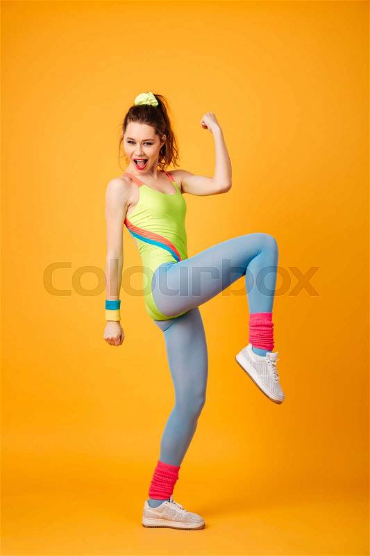Image of happy young fitness lady posing over yellow background. Looking at camera make winner gesture, stock photo