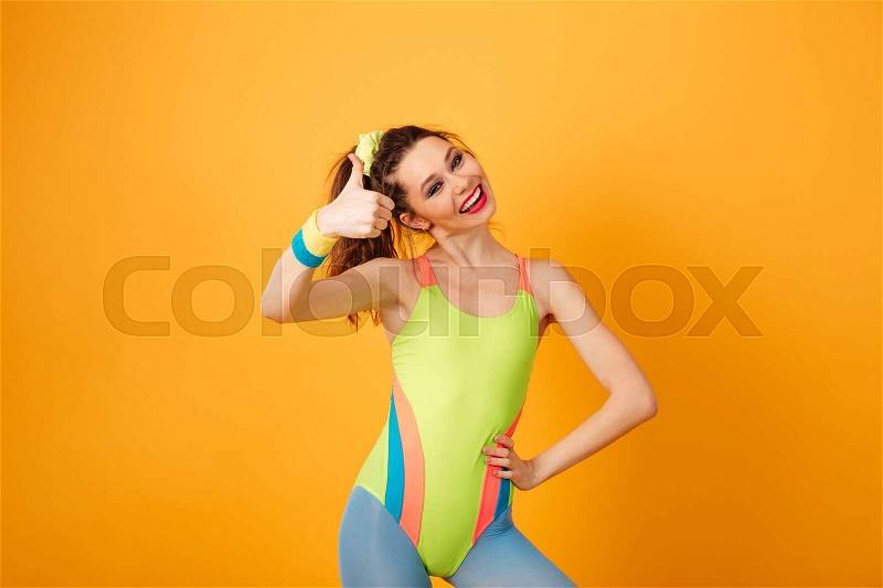 Image of cheerful young fitness lady posing over yellow background. Looking at camera make thumbs up gesture, stock photo